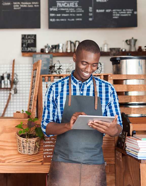 A man in an apron is using a tablet in a coffee shop at Queen St East in Scarborough, ON