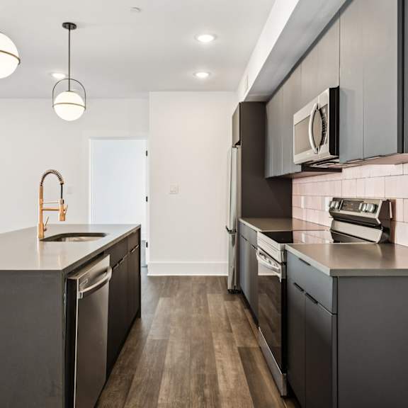 A modern kitchen with dark wood floors and stainless steel appliances.