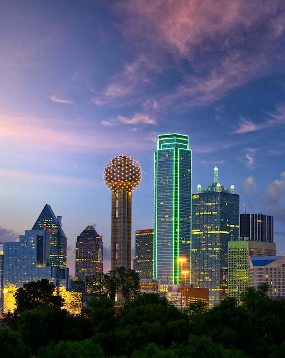 A city skyline at dusk with the sun setting behind the buildings.