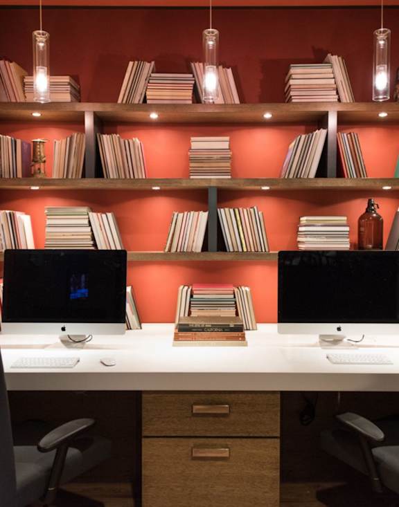 A desk with two computers and a bookshelf with books.