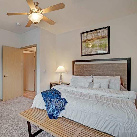 The master bedroom has a king-sized white bed and a ceiling fan with a walk-in closet at Swan Creek Apartment Homes. 