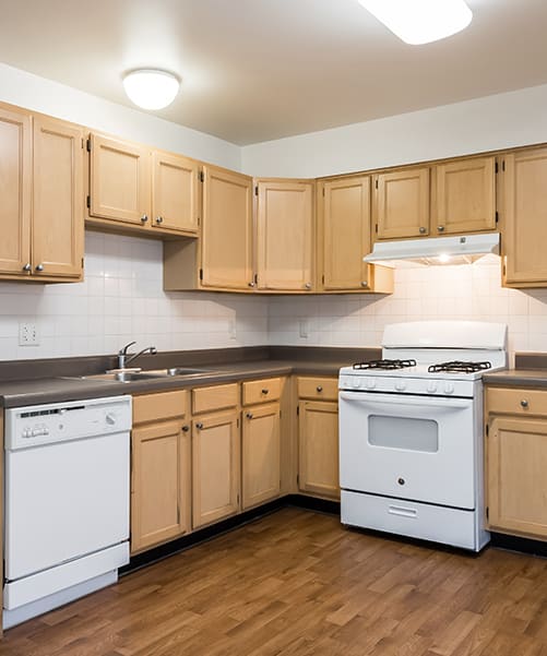 A kitchen with light wood cabinets, white appliances and wood flooring at Duneland Village apartments & Townhomes in Gary, IN