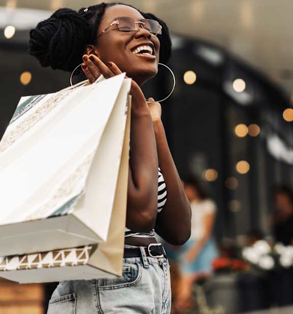 A woman is holding shopping bags and smiling.