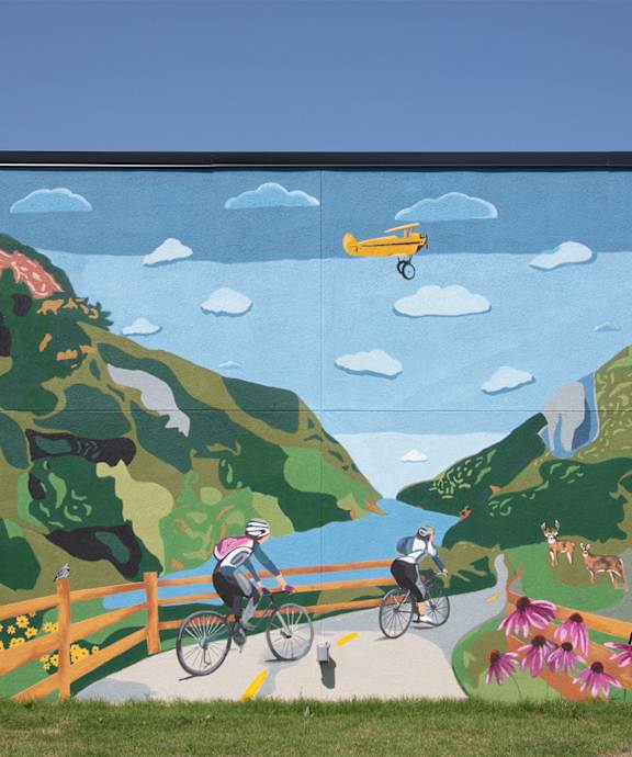 A mural depicts a cyclist and a pedestrian on a path through a mountainous landscape.