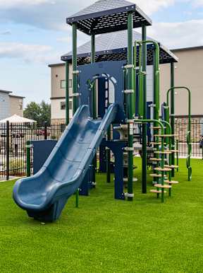 A playground with a green slide and a black fence.
