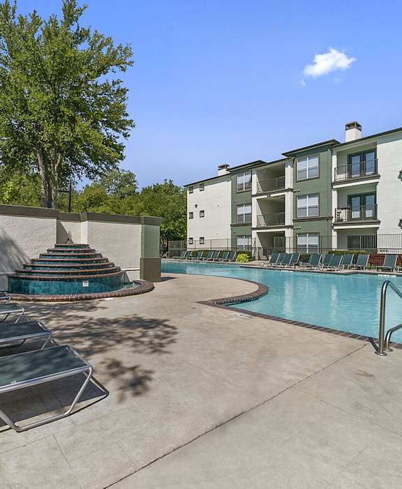 A pool area with sun loungers and a building in the background.