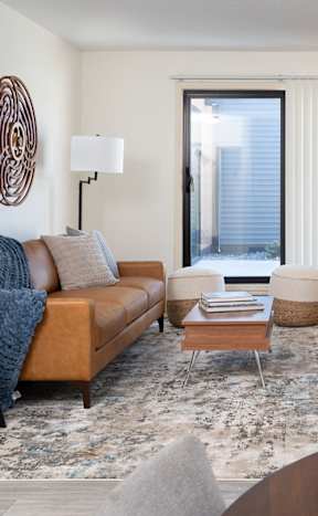 A living room with a brown sofa, a wooden coffee table, and a TV on a cabinet at The Bosk Apartment Homes, Minnesota 55125