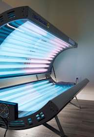 A tanning bed with a blue light is in a room with a chair.