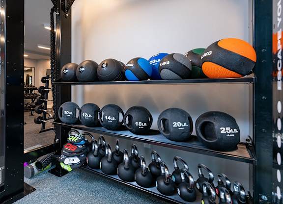 A gym with a rack of kettlebells and a yellow pull up bar.