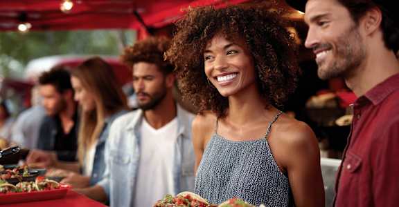 A group of people are standing around a table with food on it.
