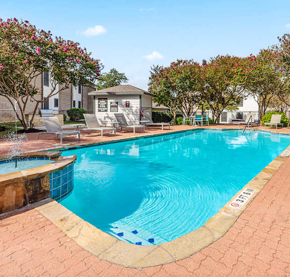 A swimming pool surrounded by a brick patio and lounge chairs.