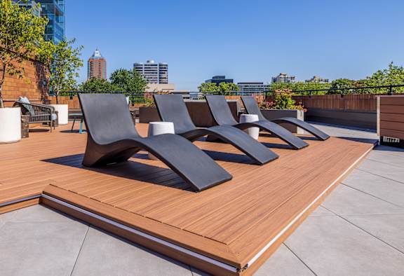 a row of black lounge chairs on a wooden deck on a roof