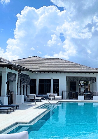 A large swimming pool in front of a white building with a black roof.
