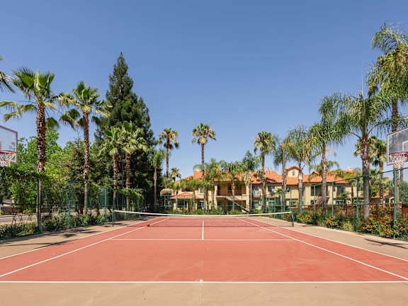 A red clay tennis court surrounded by palm trees.
