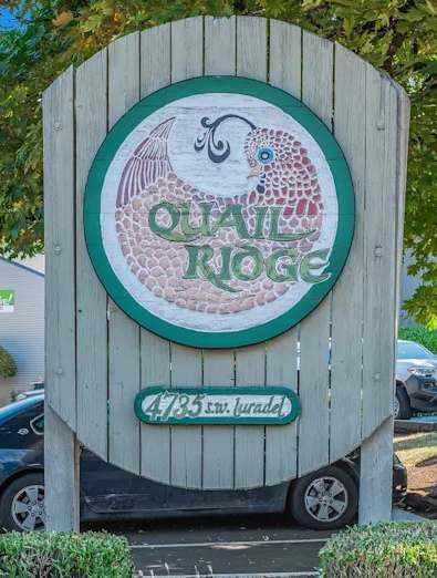 A sign for a Quail Ridge is in front of a white fence and green bushes.