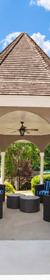 A gazebo with a brown roof is surrounded by green bushes and trees.