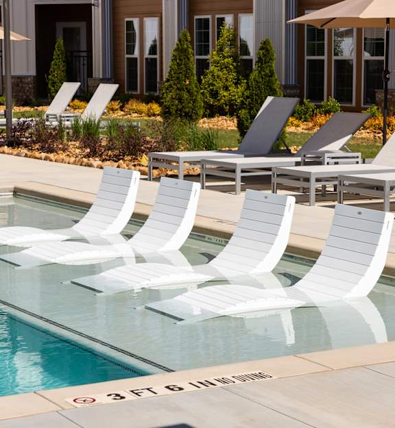 A pool with white chairs and a building in the background.