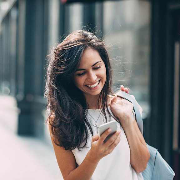 A woman is standing on a street holding a phone in her hand.