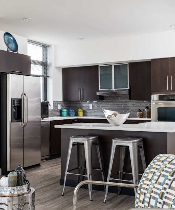 A modern kitchen with a refrigerator, stove, and bar stools.