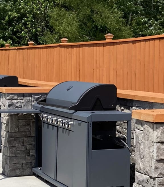 a row of barbecue pits on a stone retaining wall with a wooden fence