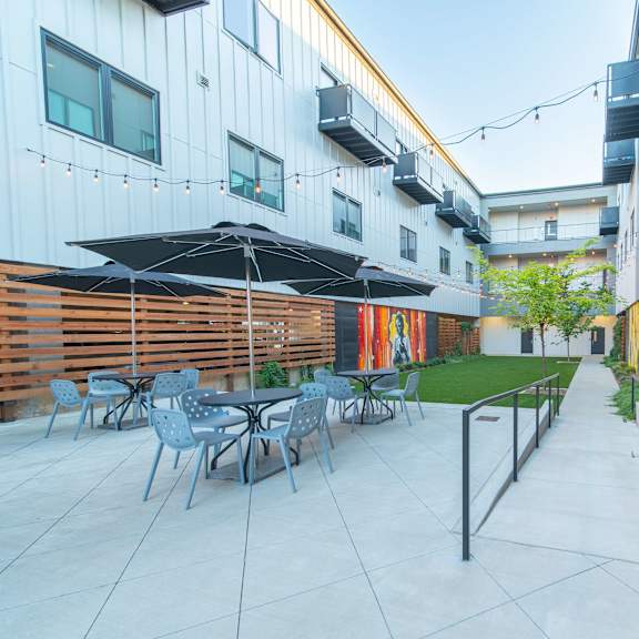 A patio with chairs and umbrellas is surrounded by buildings.