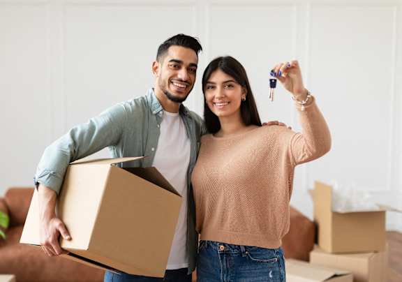 A man and woman are standing in a room with boxes, holding a key and a box.