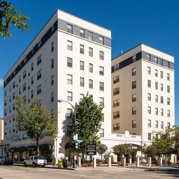 A brick building with a balcony and a tree in front. at Columbia Uptown Apartments, Washington, Washington DC