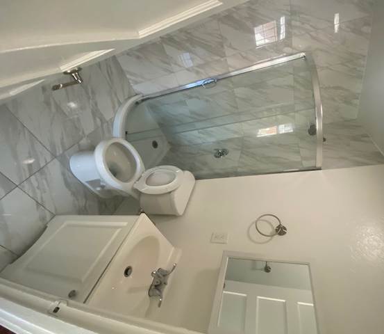 A white toilet with a bidet attachment is in a bathroom with marble flooring and a glass shower door.