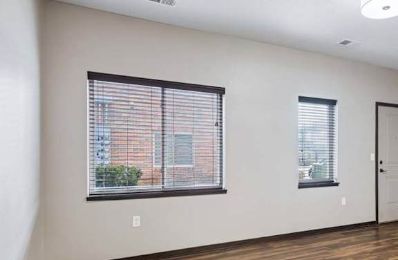 Spacious living room with wood-style flooring, large windows, and an open layout connected to the kitchen area.