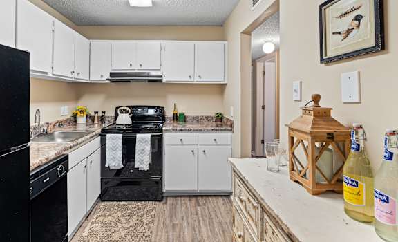 A kitchen with a black fridge, white cabinets, and a black stove top.