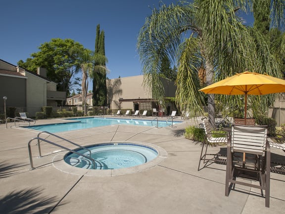 River Pointe apartments spa and pool area with palm trees, lounge chairs, table and sun umbrella 