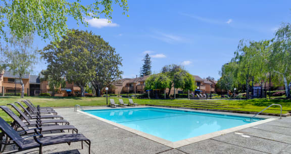 a swimming pool with chaise lounge chairs and trees in the background