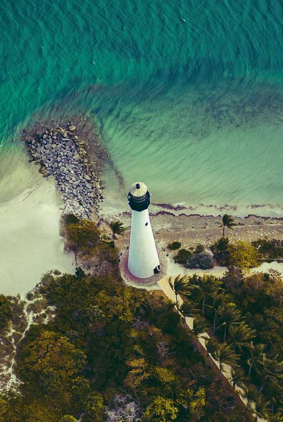 A lighthouse stands on a cliff overlooking a beach.