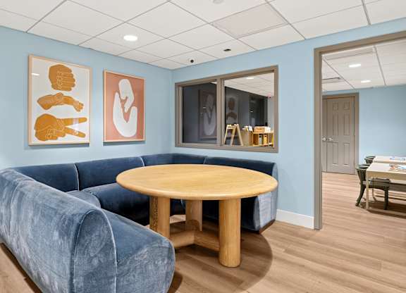 A blue couch sits in a room with a wooden table and two framed artworks on the wall.