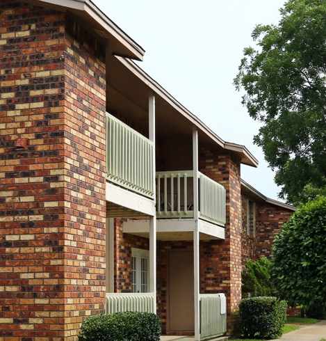 A brick building with a red flower bush on the left.