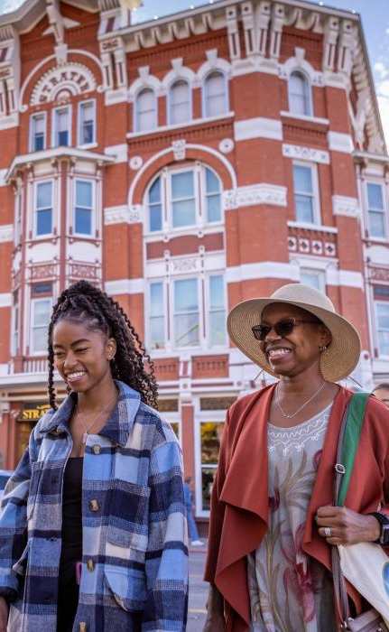 Two people walking on a street in front of a red building.