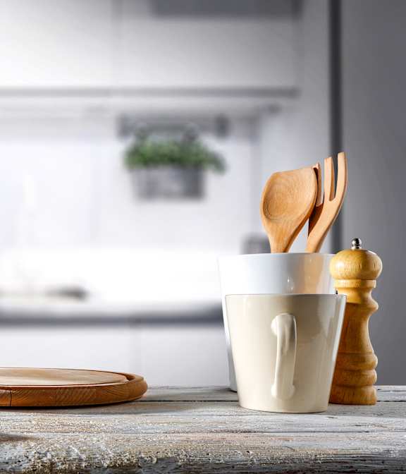 A kitchen counter with a cup, a plate, a wooden spoon, and a pepper grinder.
