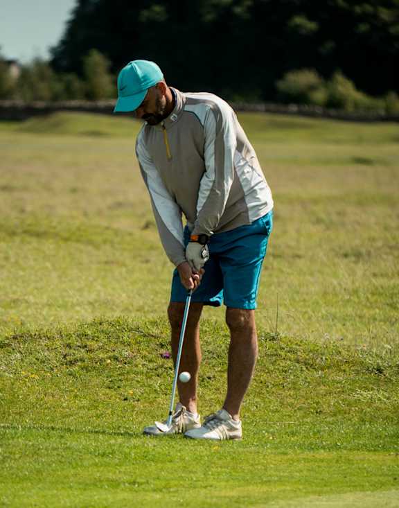 A man in a teal cap and white shirt is playing golf.