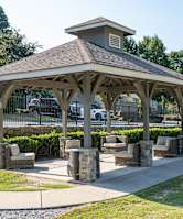 A gazebo with a stone pillar and a roof is surrounded by a fence and a grassy area.