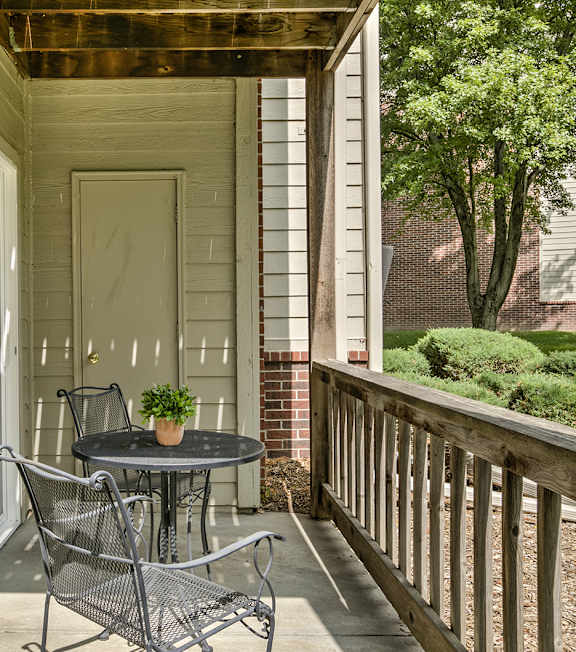 A small table with two chairs is on a porch.