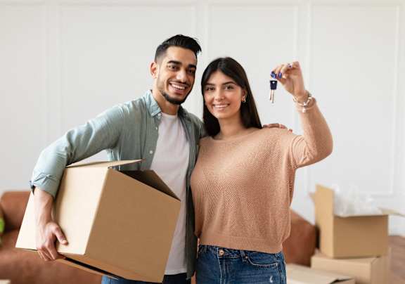 A man and woman are standing in a room with boxes, holding a key and a box at River Stone Ranch, Austin, Texas