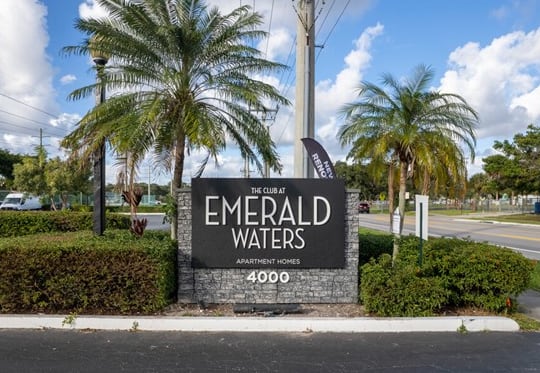 a sign that reads emerald waters with palm trees in the background