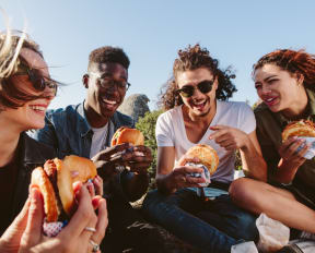 Group of Friends Sitting in Circle Outside Eating Burgers