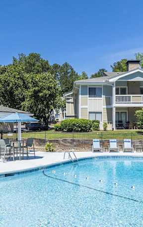 A swimming pool in front of a house with a blue umbrella.