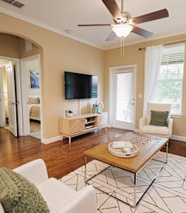 A living room with a white couch, a wooden coffee table, and a flat screen TV mounted on the wall.