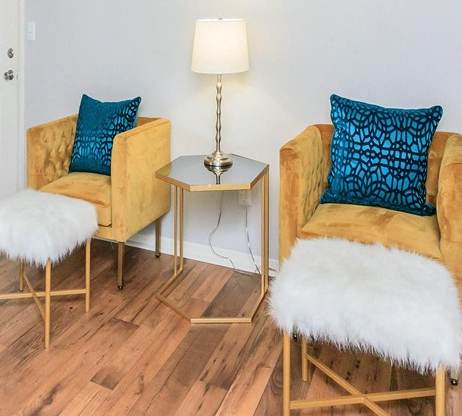 Two yellow chairs with blue cushions and white fur on the armrests are in a room with wooden floors.
