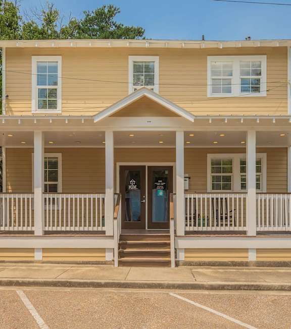 A yellow house with a porch and a white fence. at The Cove at State Street Apartments, Baton Rouge, LA, 70802