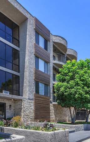 A swimming pool in front of a building with yellow chairs around it. at Lafayette Apartments, Los Angeles 90019