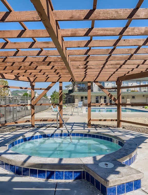 our hot tub is under a wooden pergola with a pool