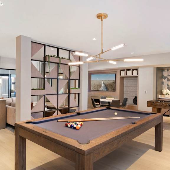A pool table is in the middle of a room with a bar and a TV.